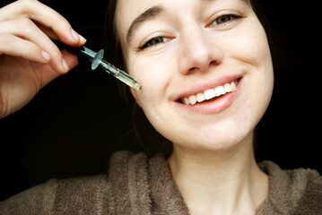 Beauty and skin care concept. Woman's face applying tea tree facial serum.
A beautiful young natural girl without makeup applies a serum to her face with a pipette.