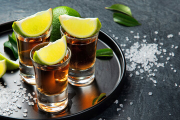 Tequila shots with lime and salt on gray background.