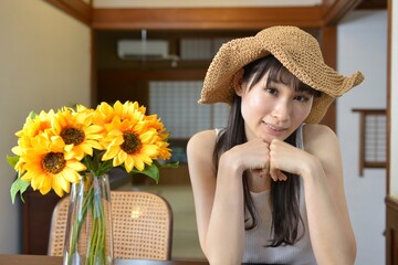 古民家の和室にてひまわりの花束と麦わら帽子を被った微笑む若い女性