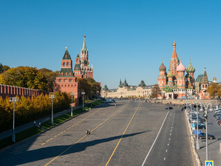 Obraz premium View of the Kremlin and St. Basil's Cathedral from the Moskvoretsky bridge against the blue sky. People walk along Red Square. Moscow, Russia.