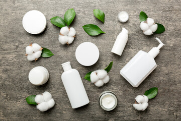 Organic cosmetic products with cotton flower and green leaves on cement background. Flat lay
