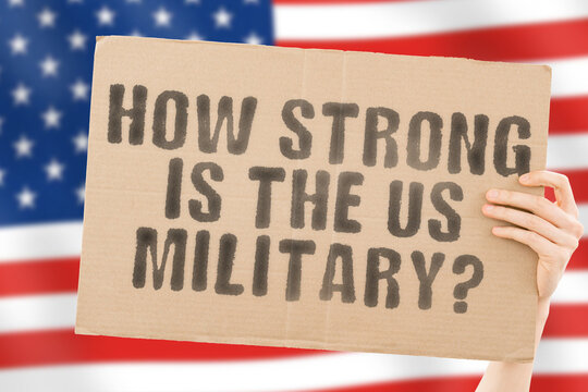 The question " How strong is the US military? " on a banner in men's hand with blurred American flag on the background. Protection. Security. Guard. Armour. Defence. Weapon. Powerful. Mighty