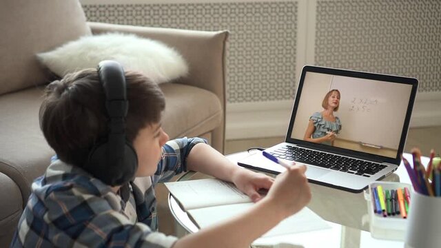 Online primary school education. Attentive kid in checkered shirt listens to teacher showing sums at blackboard on monitor at video lesson at home spbas spbd