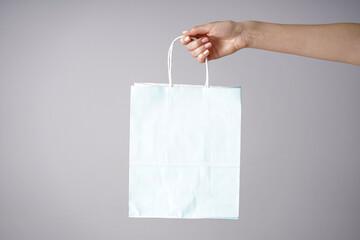Paper blue bag in a female hand on a gray background, place for text.