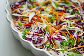Coleslaw cabbage salad with cabbage, carrots, herbs and sesame seeds on a white plate. Healthy eating, vegan food