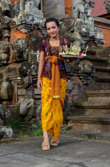 Fototapeta na wymiar Portrait of beautiful Balinese girl inside old temple in Bali, with a traditional clothing and carrying offerings.