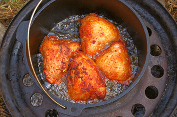 Chicken thighs cuts fried in a cast iron cauldron. Chicken meat cooked al fresco on a recycled car rim.