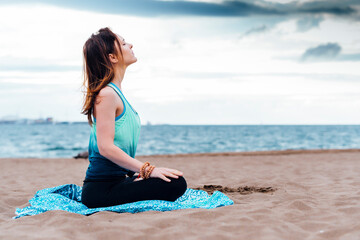 Fototapeta na wymiar young adult woman doing youga meditating on the beach on cloudy day