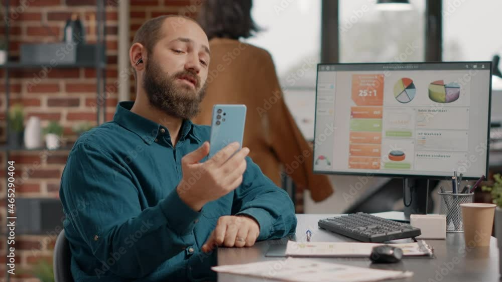 Poster employee holding smartphone to talk on video call with colleagues in startup office. business man us
