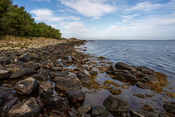Fototapeta na wymiar A rocky shoreline with blue water and a blu sky in the background. Picture from Skalderviken, southern Sweden