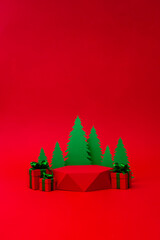 Green Christmas tree with red gift box with green ribbon and pedestal on the red background. Christmas creative concept. Place for text.