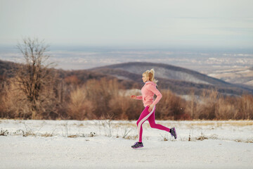 Sportswoman in shape jogging in nature at snowy winter day. Healthy habits, winter fitness, cardio...