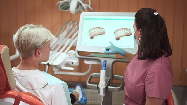 Orthodontist consults teenager patient. Woman dentist with mask shows jaws model on computer screen to spbd senior schoolboy during appointment in hospital office