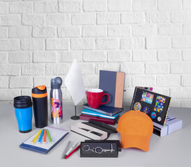 Composition of different promo products - Thermo mug, mug, gifts, pens in boxes, notebooks, tools, cap,flag table. Copy space. Grey wall background. - obrazy, fototapety, plakaty