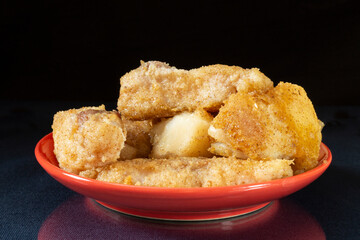 A piece of fried fish in a red plate on the table with a reflection.