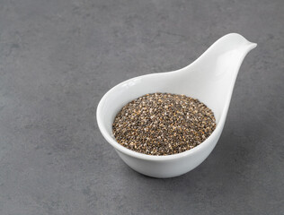 Chia seeds in a white bowl over stone background with copy space