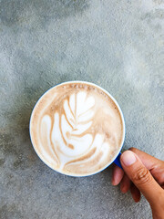 hand holding Hot coffee latte art in a cup on a grey cement background.