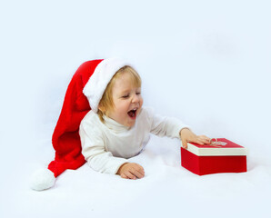 A happy child in a Santa Claus hat lies on a light background and rejoices at the gift. The concept of New Year and Christmas. place for text, flyer, advertisement