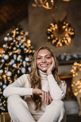 young beautiful woman model with long hair in a beige suit christmas tree christmas In brown wooden houses 