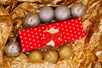 Christmas decorated gift with red and white dots on paper with red tassels and Christmas tree ball decorations isolated on a shiny orange background with bokeh. Merry Christmas
