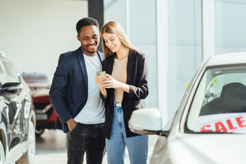 Multiracial couple using mobile while choosing car at salon