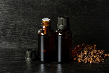 Essential oil of cloves in bottle and dry cloves on wooden bowl on black wooden background dark tone.