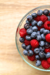 Glass bowl filled with raspberries and blueberries on wooden table. Top view.