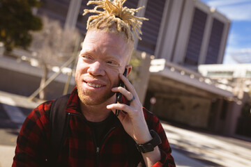 Happy albino african american man with dreadlocks talking on smartphone