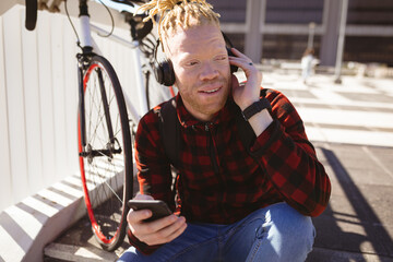 Happy albino african american man with dreadlocks wearing headphones using smartphone