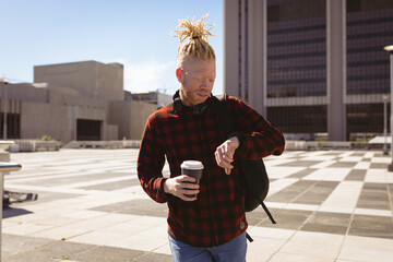 Thoughtful albino african american man with dreadlocks using smartwatch