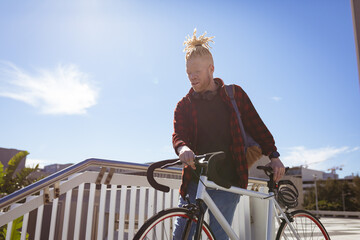 Thoughtful albino african american man with dreadlocks going down stairs with bike