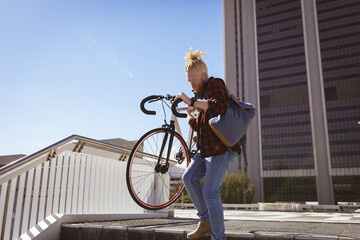 Thoughtful albino african american man with dreadlocks going down stairs with bike
