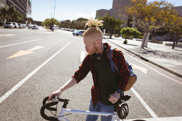 Thoughtful albino african american man with dreadlocks crossing road with bike