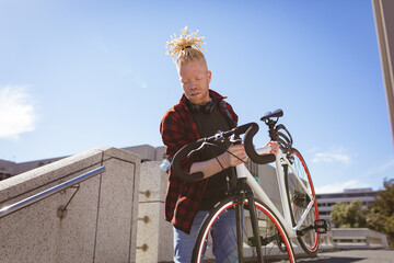 Thoughtful albino african american man with dreadlocks going down stairs with bike