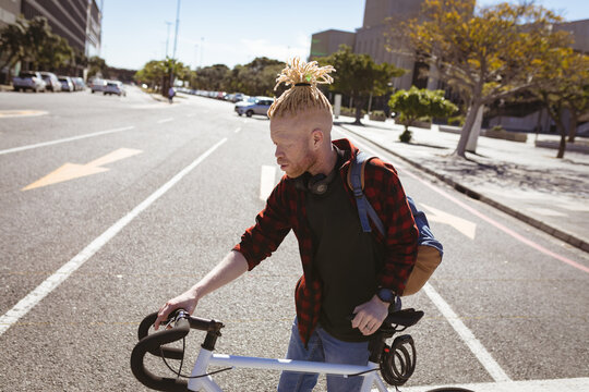 Thoughtful albino african american man with dreadlocks crossing road with bike