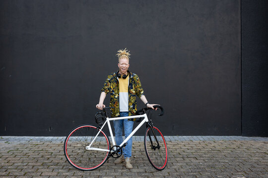Portrait of smiling albino african american man with dreadlocks on street with bike