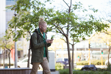 Thoughtful albino african american man with dreadlocks walking using smartphone