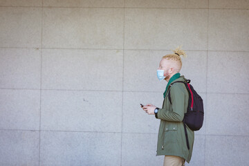 Albino african american man with face mask and dreadlocks walking and using smartphone