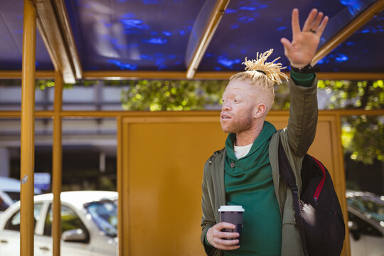Albino african american man with dreadlocks holding takeaway coffee and waving