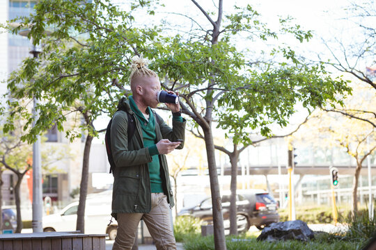 Thoughtful albino african american man with dreadlocks drinking coffee using smartphone - Powered by Adobe