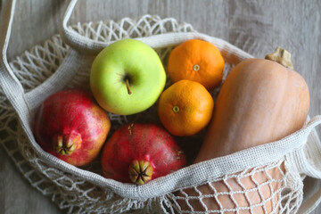 Crochet bag filled with butternut squash, pomegranates, apples and tangeriens. Top view.