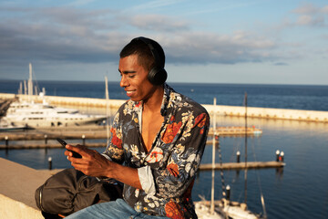 Cheerful guy with the headphones. Young african man listening the music outdoors..