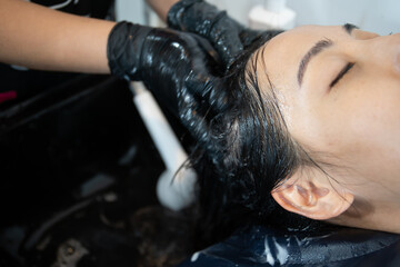 Beautiful Asian young woman having a hair care treatment and hair washing service at hair salon.