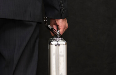 A man in a suit with a suitcase handcuffed on a black background, close-up, selective focus, dark...