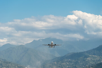 Fototapeta na wymiar Passenger plane took off from the airport near the mountains. Plane flies against the background of the sky with clouds, mountains, private houses. Travel