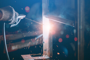 A steelworker is welding a structure in a factory with safety equipment. The concept of maintenance of construction with skilled labor.
