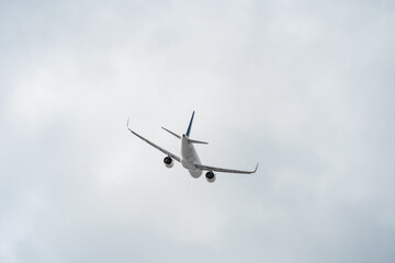 Rear view of a white passenger plane in close-up against a gray sky with copy space. Plane is heading to the right