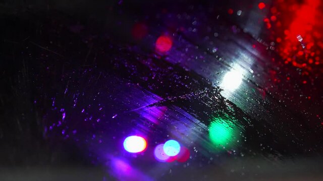 Wipers wipe the windshield from water. Bokeh of police flashing lights on background