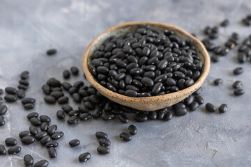 Ceramic bowl full of dry black beans on grey table closeup