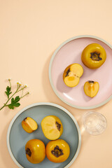 Top view of blue and pink dish of persimmon , pork , knife , water glass , flowers in light pink background for food advertising
